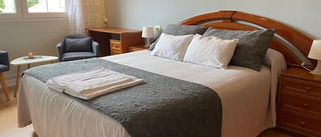 A neatly arranged hotel room with a large bed, a desk, a chair, and a small table.