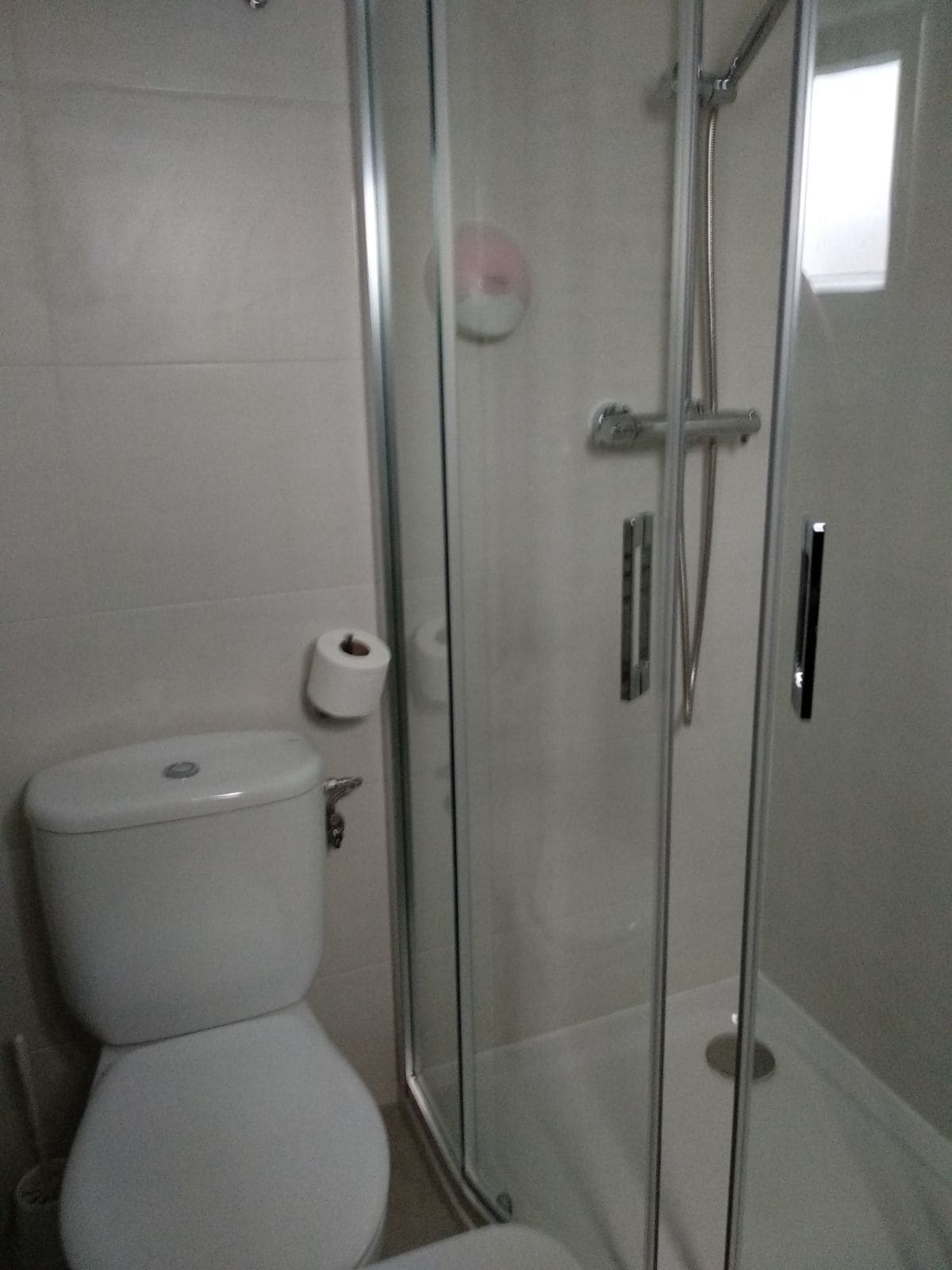 A bathroom with a toilet, a glass shower enclosure, and a toilet paper roll.