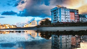 A waterfront cityscape with buildings reflected in calm water. - Hostal Buenavista (Cervo)