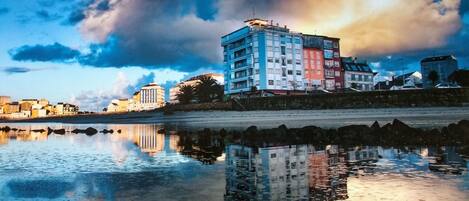A waterfront cityscape with buildings reflected in calm water.