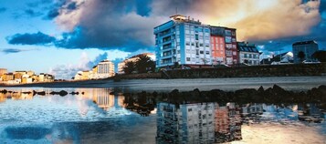 Un paisaje urbano frente al mar, con edificios reflejados en aguas tranquilas.