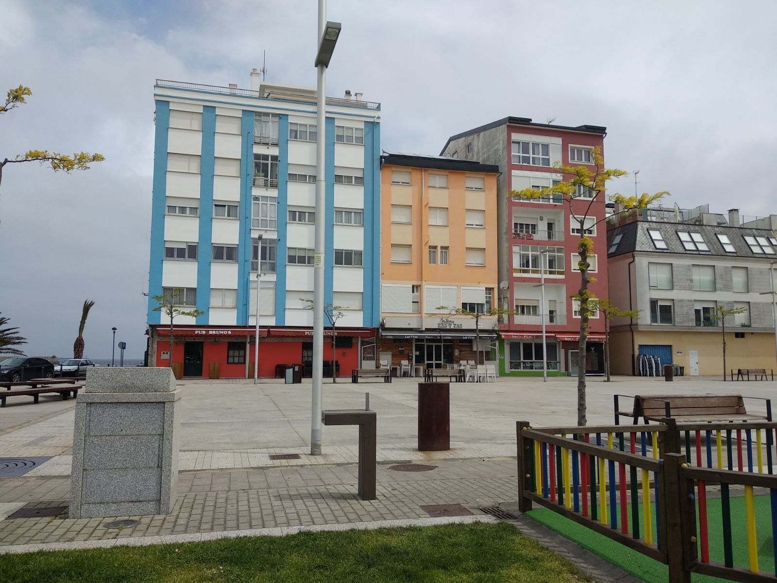 Un edifici de diverses plantes amb façana blava i blanca, un pis inferior vermell amb botigues i un teulat verd.