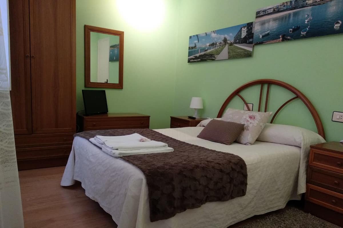 Un dormitorio con cama, mesita de noche, cómoda, espejo y una pared con dos cuadros.
