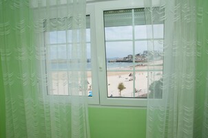 Una habitación con un ventanal grande que ofrece vistas a una playa y edificios al otro lado del agua.