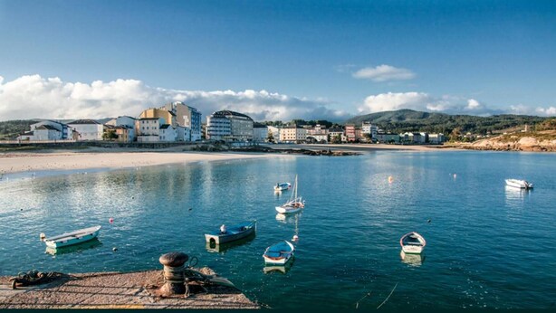 A coastal town with boats on calm water, buildings along the shore, and a clear sky. - Hostal Buenavista (Cervo)
