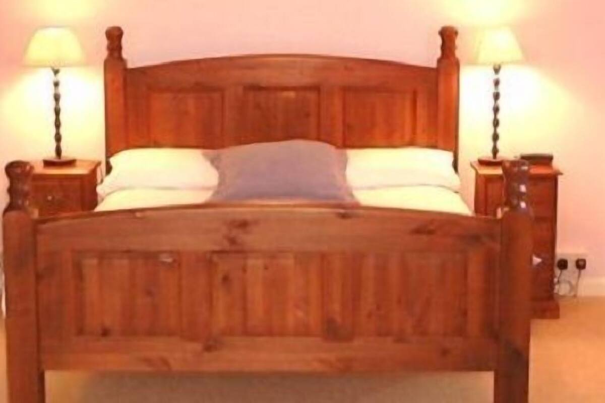 A wooden bed with two nightstands, each with a lamp, in a room with a plain wall and a door on the left.