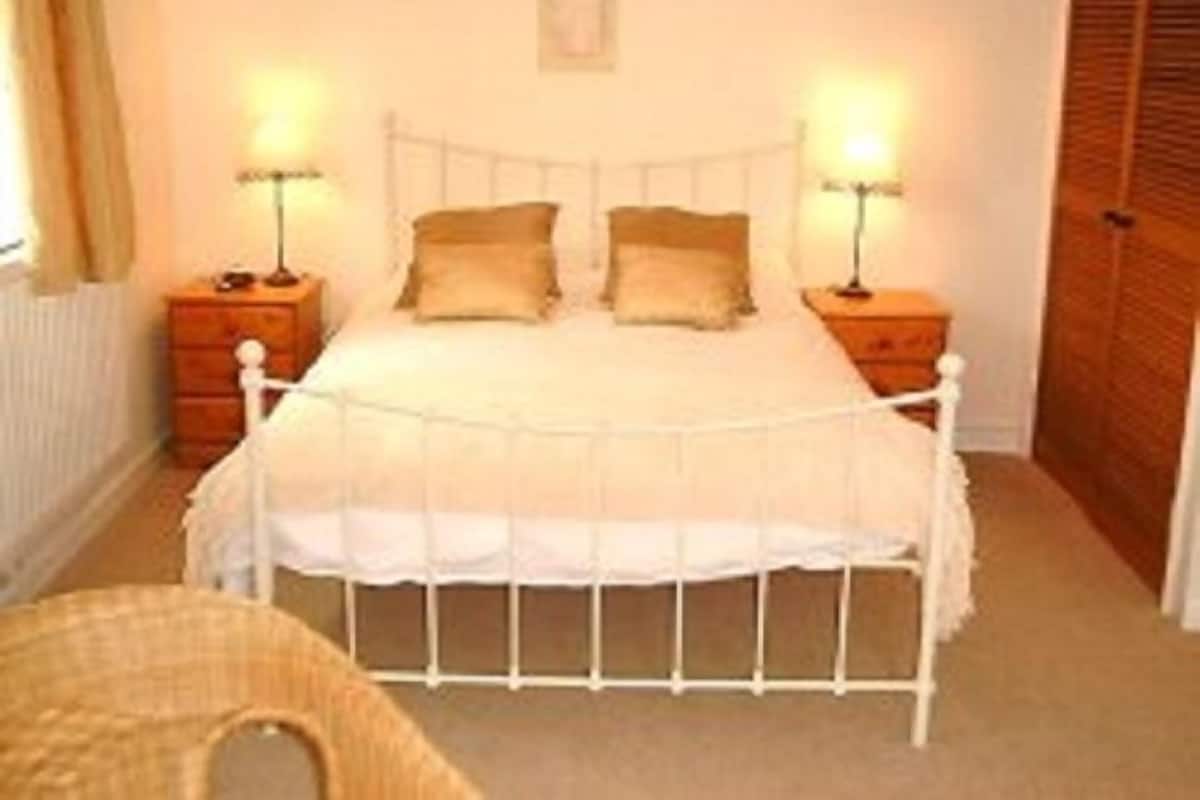 A bedroom with a white four-poster bed, two bedside tables, and a wooden wardrobe.