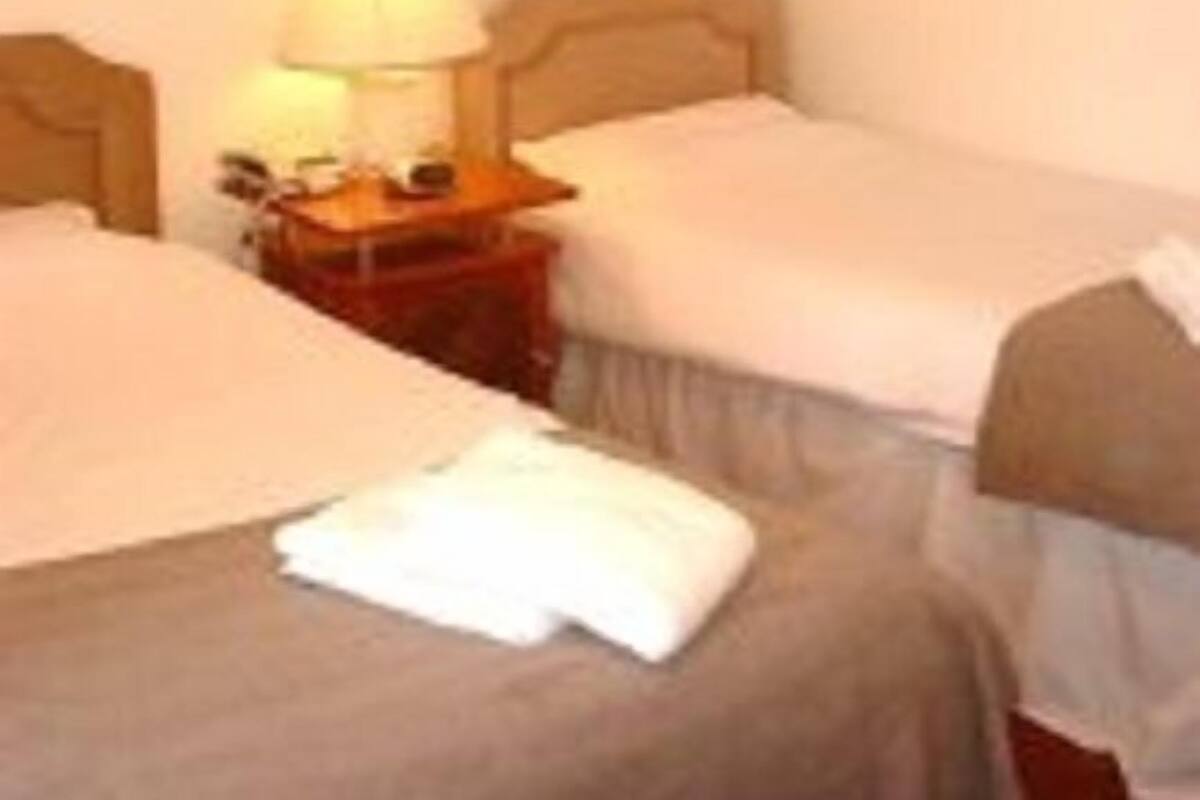 A hotel room with two beds, a nightstand with a lamp, and two framed pictures on the wall.