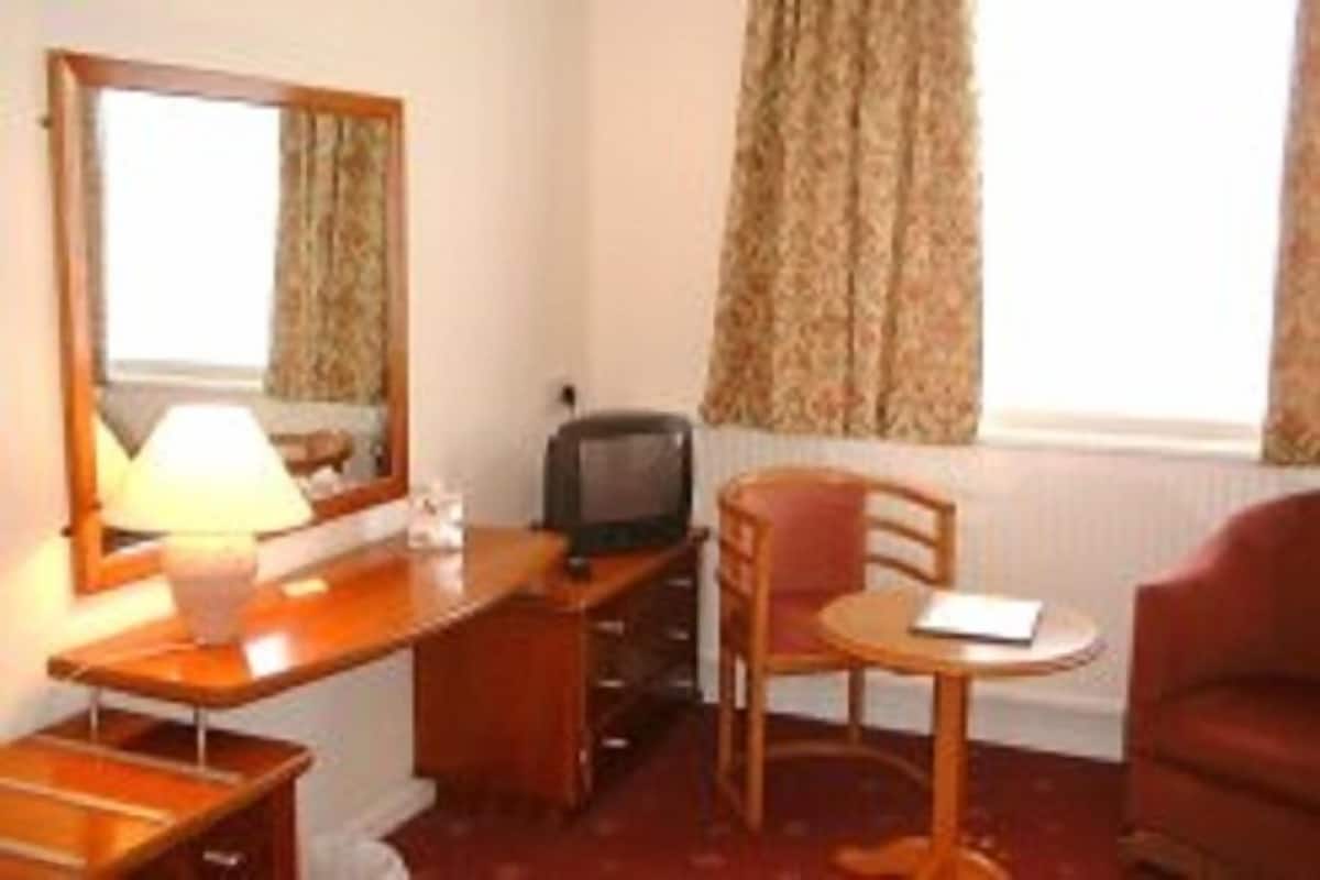A hotel room with a wooden desk, a chair, a television, and a red armchair.
