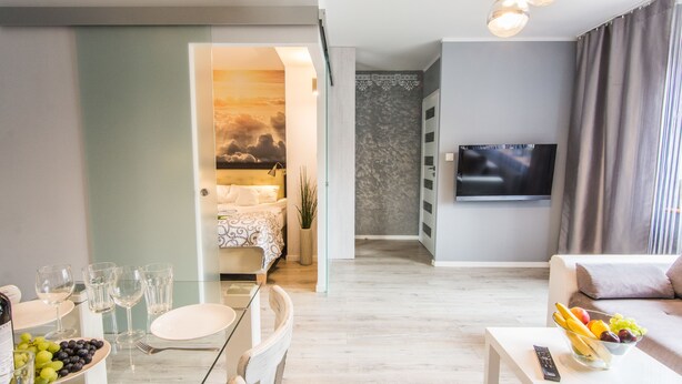 A modern living room with a flat-screen TV, a dining area with a glass table, and a bedroom with a bed and a view of the sky. - Apartamenty hoteLOVE przy Strumieniu (Karpacz)
