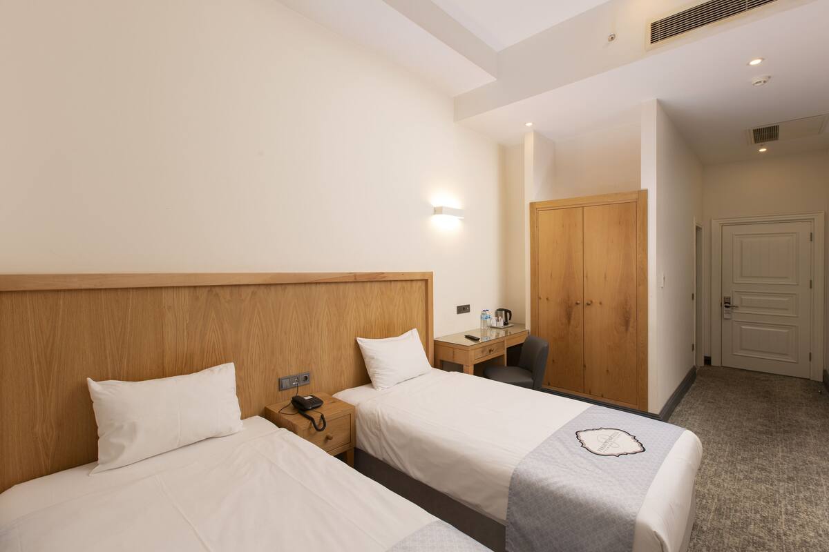 Ein Hotelzimmer mit zwei Betten, einem Schreibtisch mit Stuhl, einem Telefon und einer Tür.