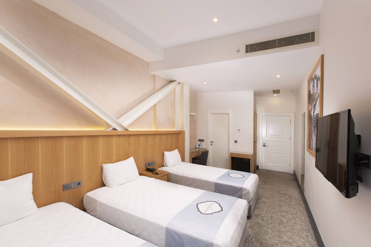 Ein Hotelzimmer mit drei Einzelbetten, einem Schreibtisch, einem Stuhl, einem Fernseher und einer Treppe.