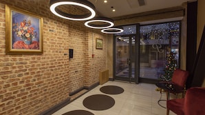 A lobby with a brick wall, a painting, circular light fixtures, a glass door, and a Christmas tree. - Premist Hotels Taksim - Special Class  (Istanbul)