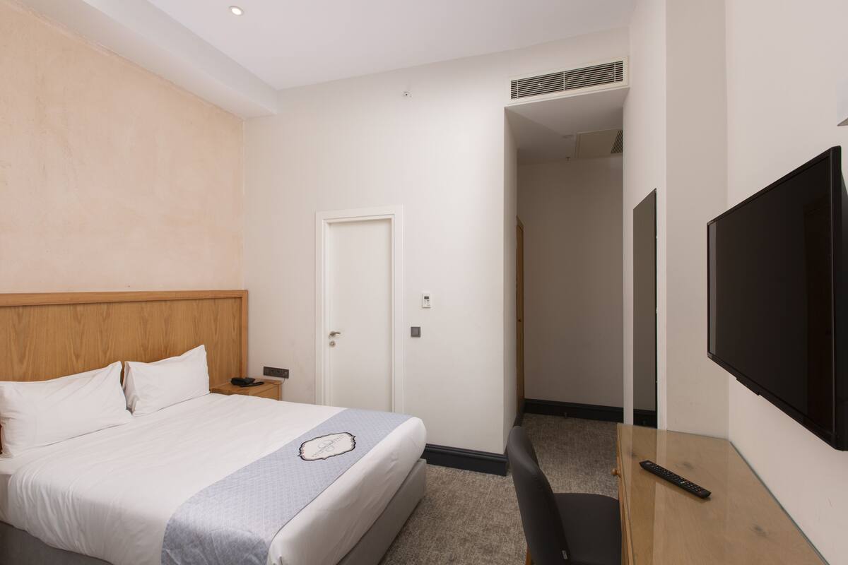 Ein Hotelzimmer mit Bett, Nachttisch, Fernseher und einer Tür zu einem anderen Raum.