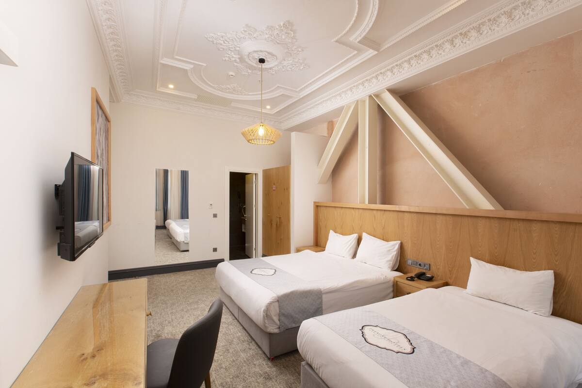 Ein Hotelzimmer mit zwei Betten, einem Holztisch, einem Fernseher und einer kunstvoll gestalteten Decke.
