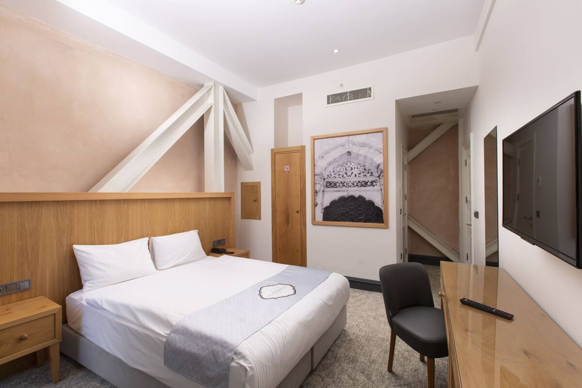 Ein Hotelzimmer mit Bett, Schreibtisch, Stuhl, Fernseher und einem gerahmten Bild an der Wand.