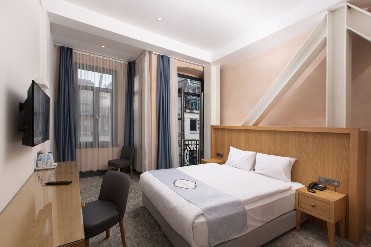 Ein Hotelzimmer mit Bett, Nachttisch, Sessel, Schreibtisch, Fernseher und Blick ins Freie.