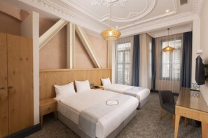 Quarto de hotel com duas camas, uma escrivaninha, uma cadeira e uma televisão.