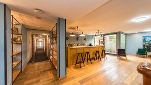 A spacious kitchen with wooden flooring, a bar area with stools, and a view of the outdoors through large windows. - Urban Park Hotel (Tbilisi)