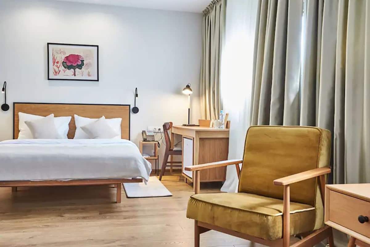 A hotel room with a bed, a desk, a chair, and a large window with curtains.