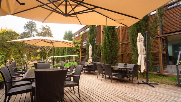 An outdoor patio area with wooden decking, black wicker chairs, and beige umbrellas. - Urban Park Hotel (Tbilisi)