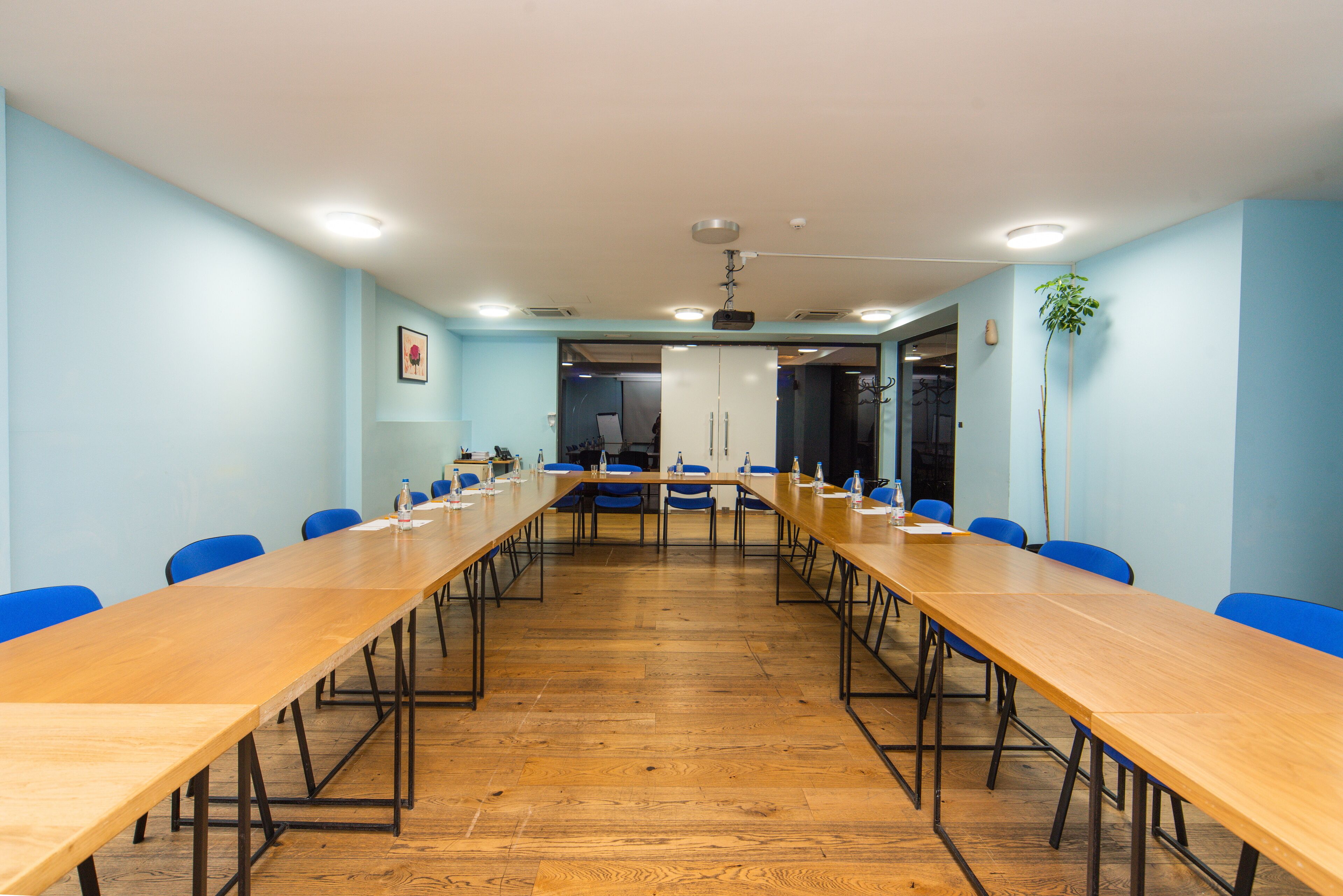 A conference room with a long wooden table, blue chairs, and a ceiling fan.