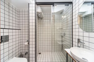 A modern bathroom with white tiled walls, a glass-enclosed shower, and a white sink.