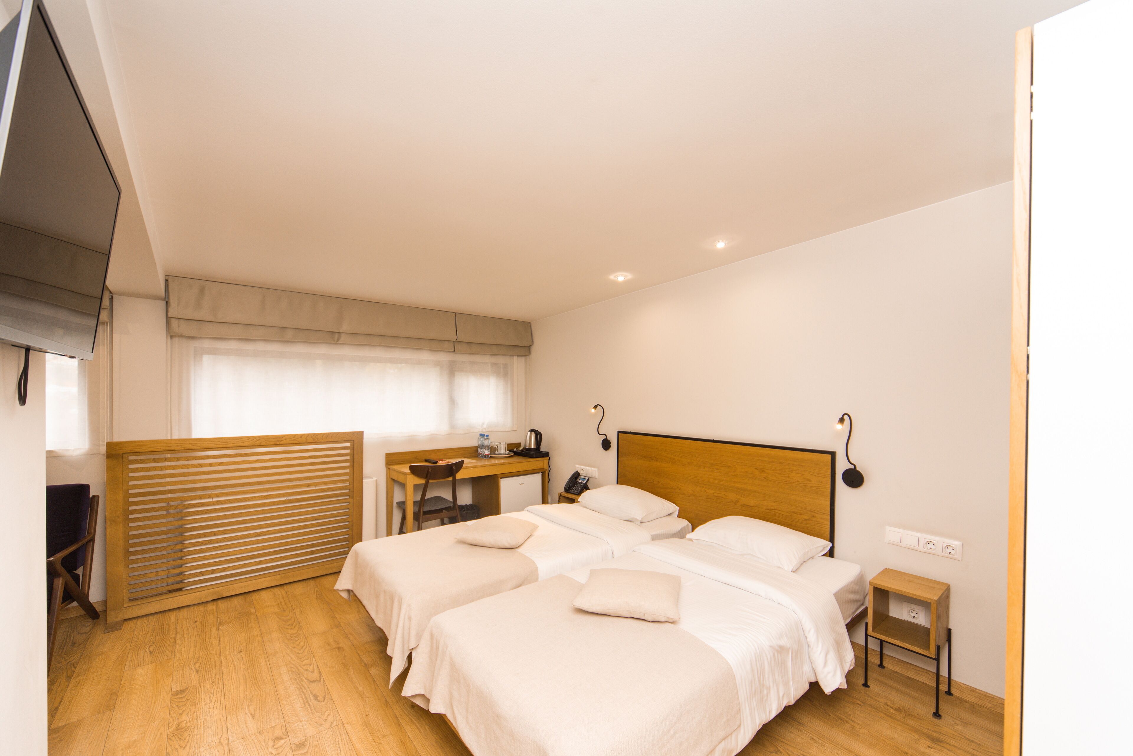Une chambre d’hôtel avec deux lits, un bureau, une chaise, une petite table et un téléviseur fixé au mur.