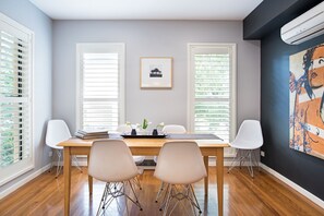 A dining area with a wooden table, white chairs, and a painting on the wall.