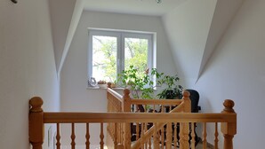 A high-ceilinged room with a wooden staircase and a large window. - Ferienwohnungen An der Sonnenwiese (Ostseebad Prerow)