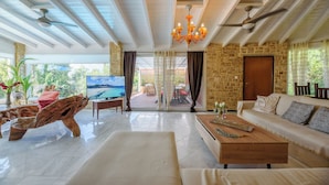 Un salon spacieux doté d’un grand téléviseur, de sièges confortables, d’une table basse en bois et offrant une vue sur la plage à travers la porte vitrée.