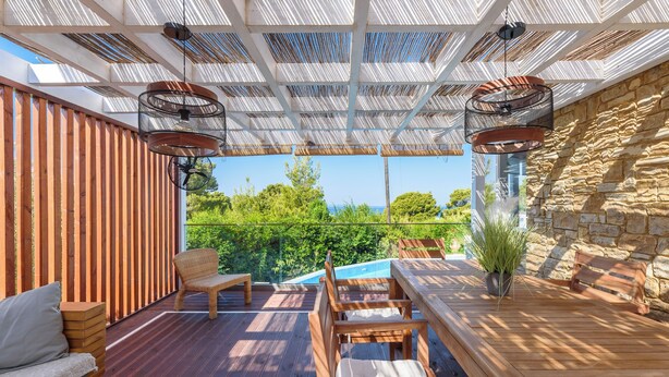 Une terrasse extérieure avec des meubles en bois, une piscine et un mur en pierre.