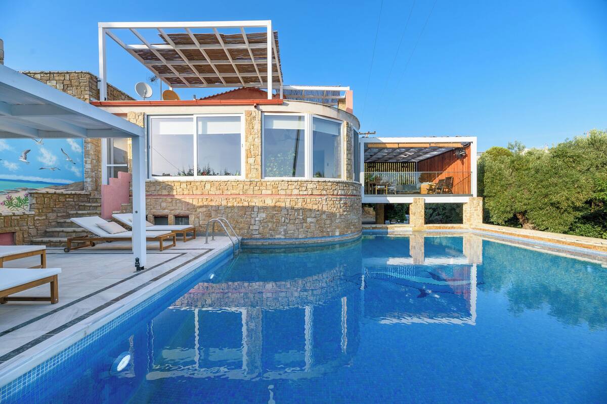 A modern poolside area with a stone wall, lounge chairs, and a clear blue pool.