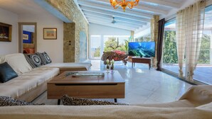 Un salon spacieux avec un mur en pierre, un plafond en bois et un grand téléviseur.