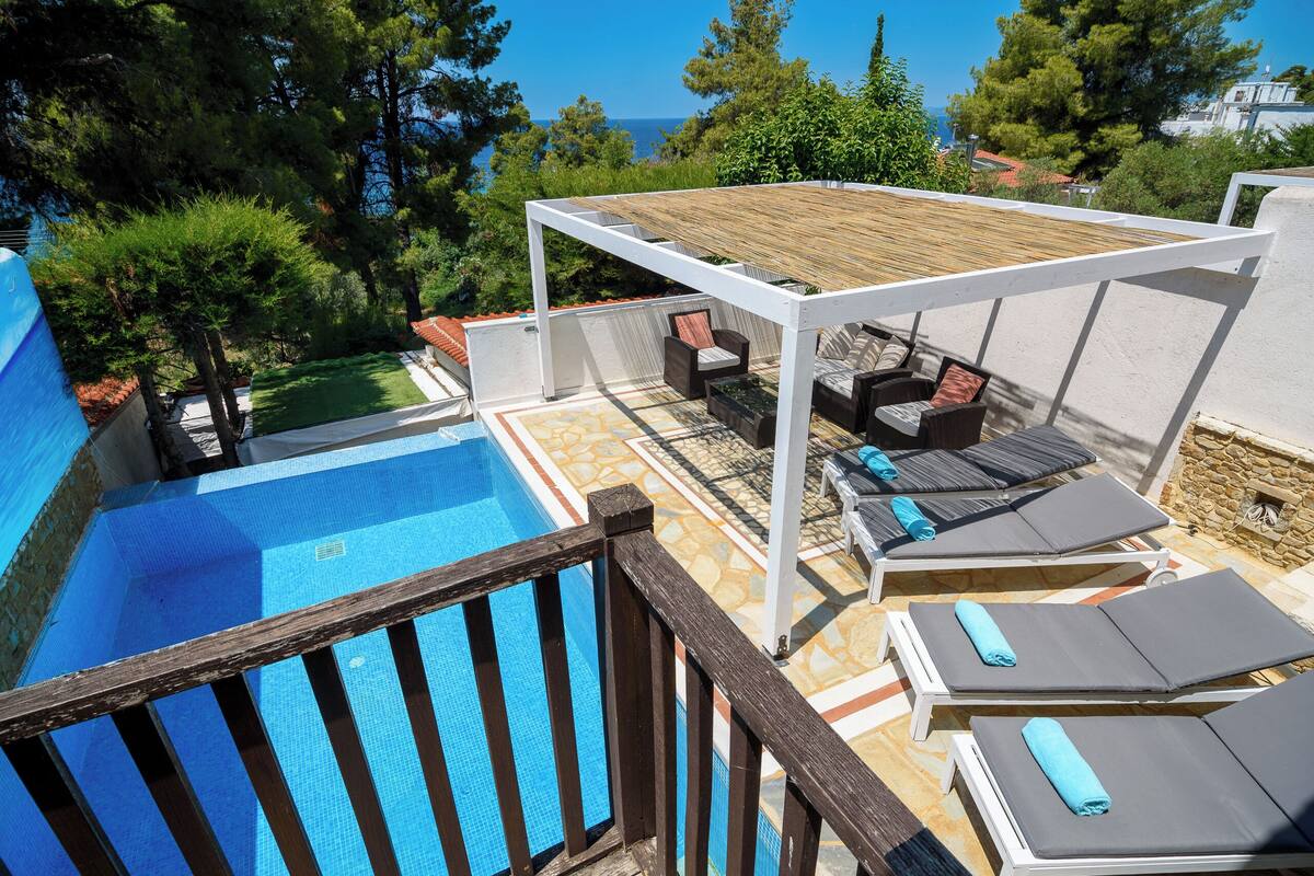 A poolside area with a pergola, lounge chairs, and a view of the sea.