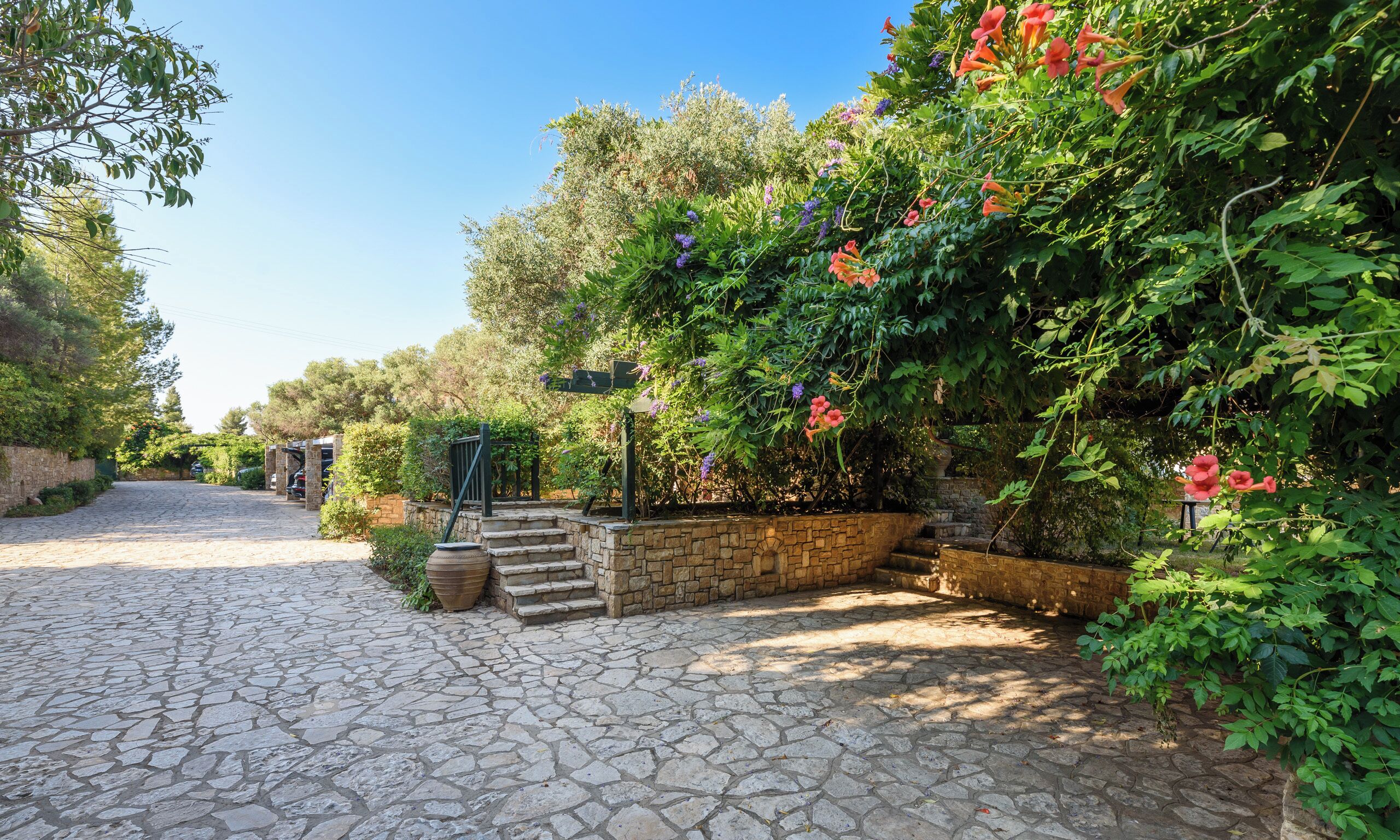 A cobblestone pathway leading to a stone staircase surrounded by lush greenery and flowering plants.