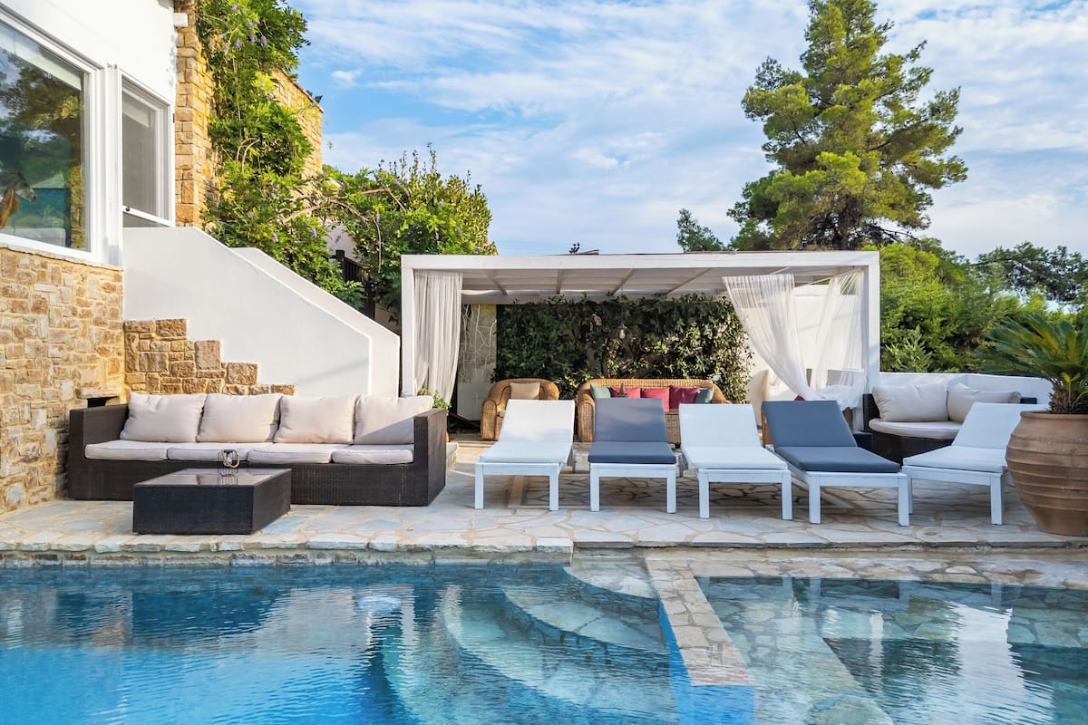 A poolside area with a stone wall, a covered seating area, and lounge chairs.