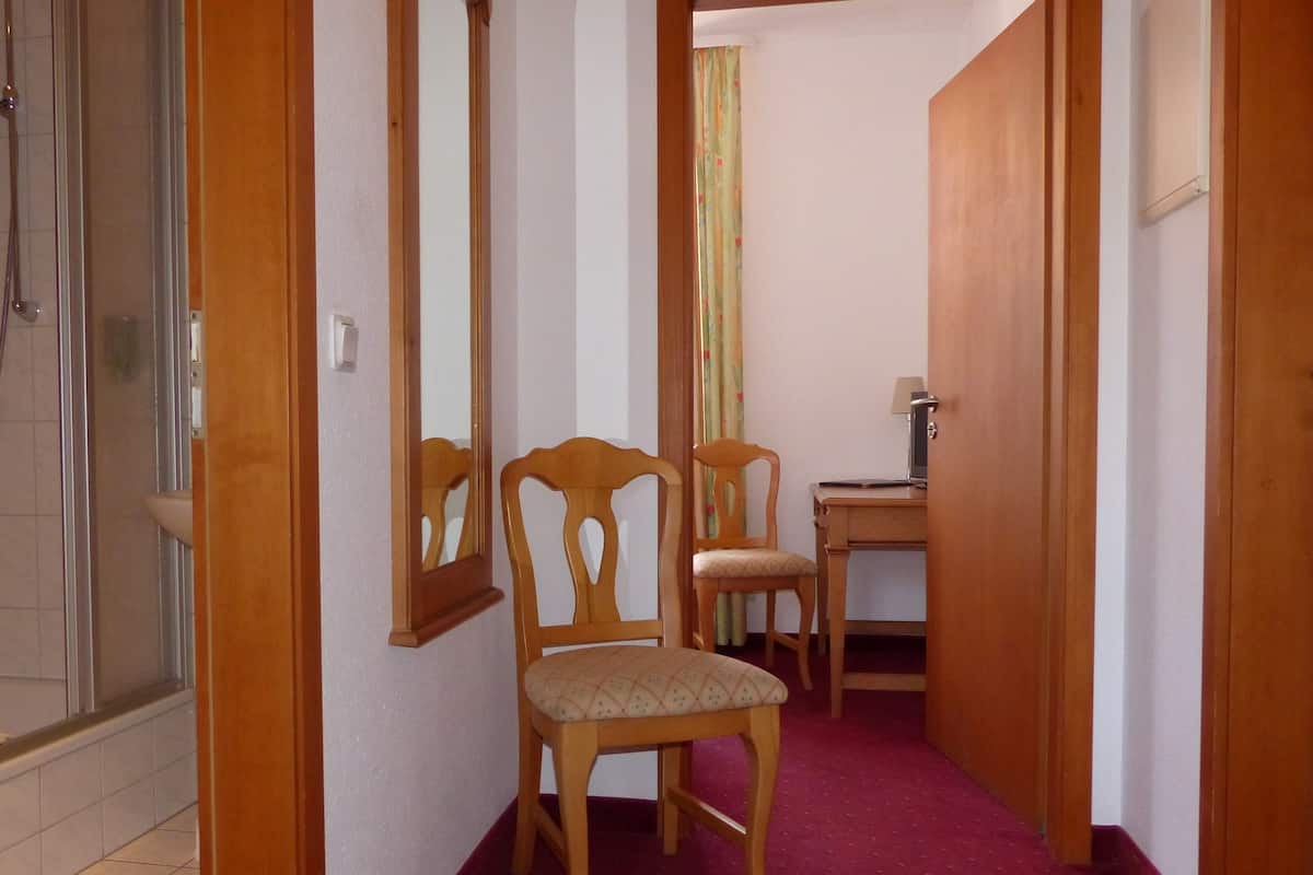 Ein enger Korridor mit einer Holztür, einem Spiegel, einem Holzstuhl und einem Schreibtisch mit einer Lampe.