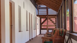 A corridor with wooden chairs, a wooden staircase, and a view of a red building outside. - Hotel zum Brauhaus Lüdde (Quedlinburg)