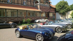A row of classic cars parked in front of a traditional half-timbered building with large windows and a brick facade. - Hotel zum Brauhaus Lüdde (Quedlinburg)
