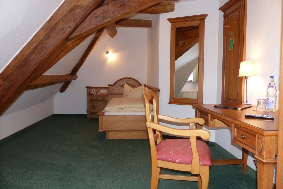 Ein Schlafzimmer mit einem hölzernen Bett, einem Schreibtisch mit Stuhl, einem Spiegel und einer Lampe.