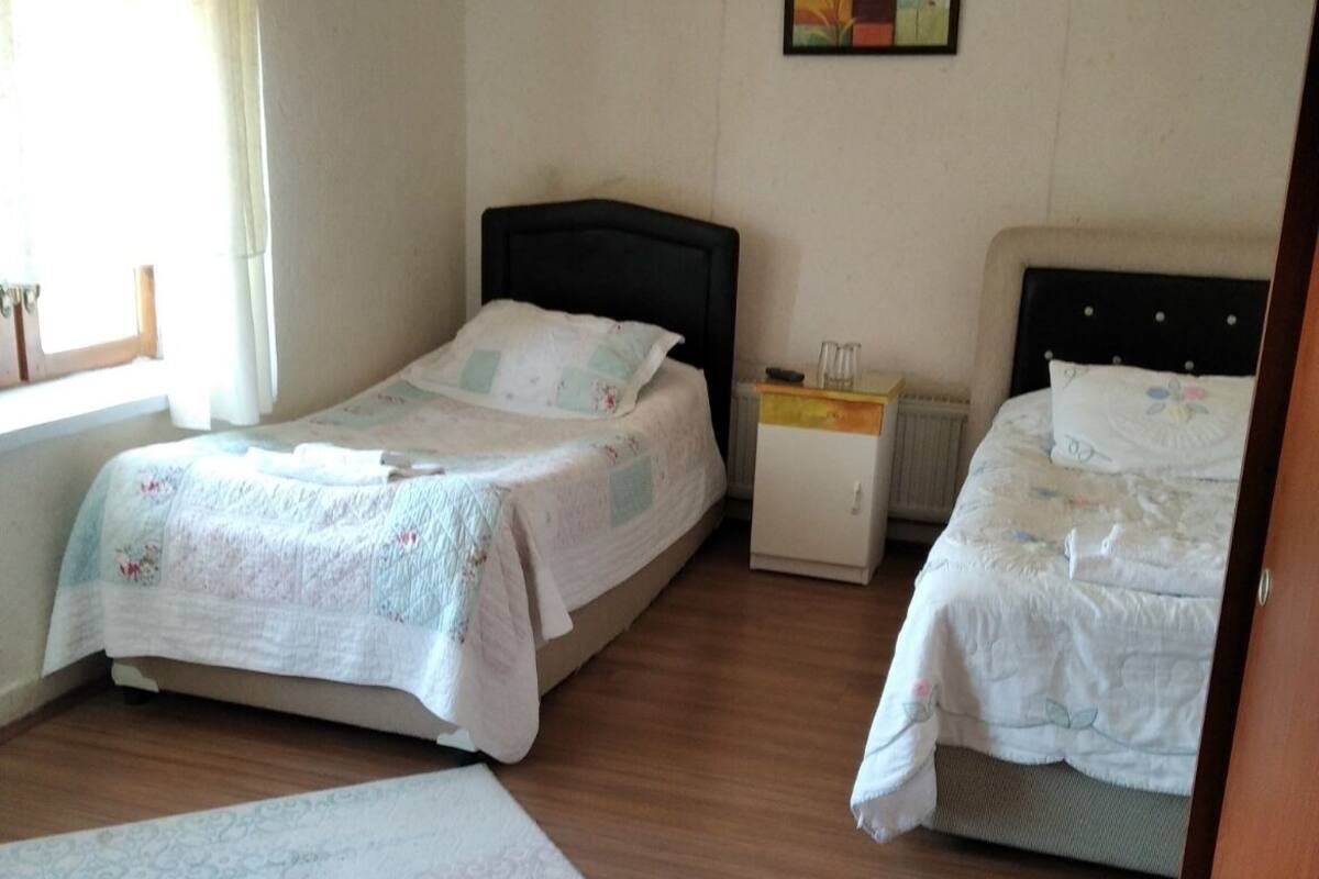 Un dormitorio con dos camas, una mesita de noche, un radiador y una ventana con cortinas.