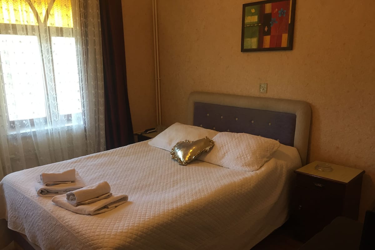 Una cama bien hecha con una colcha blanca acolchada, una almohada decorativa y toallas dobladas a un lado.