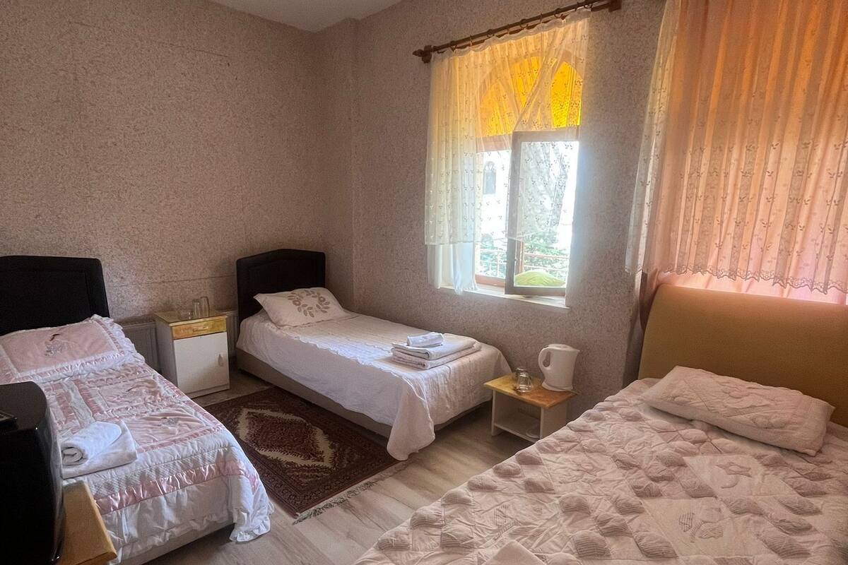 Una habitación con dos camas, una mesita pequeña, una mesita de noche, una ventana con cortinas y una lámpara en el techo.