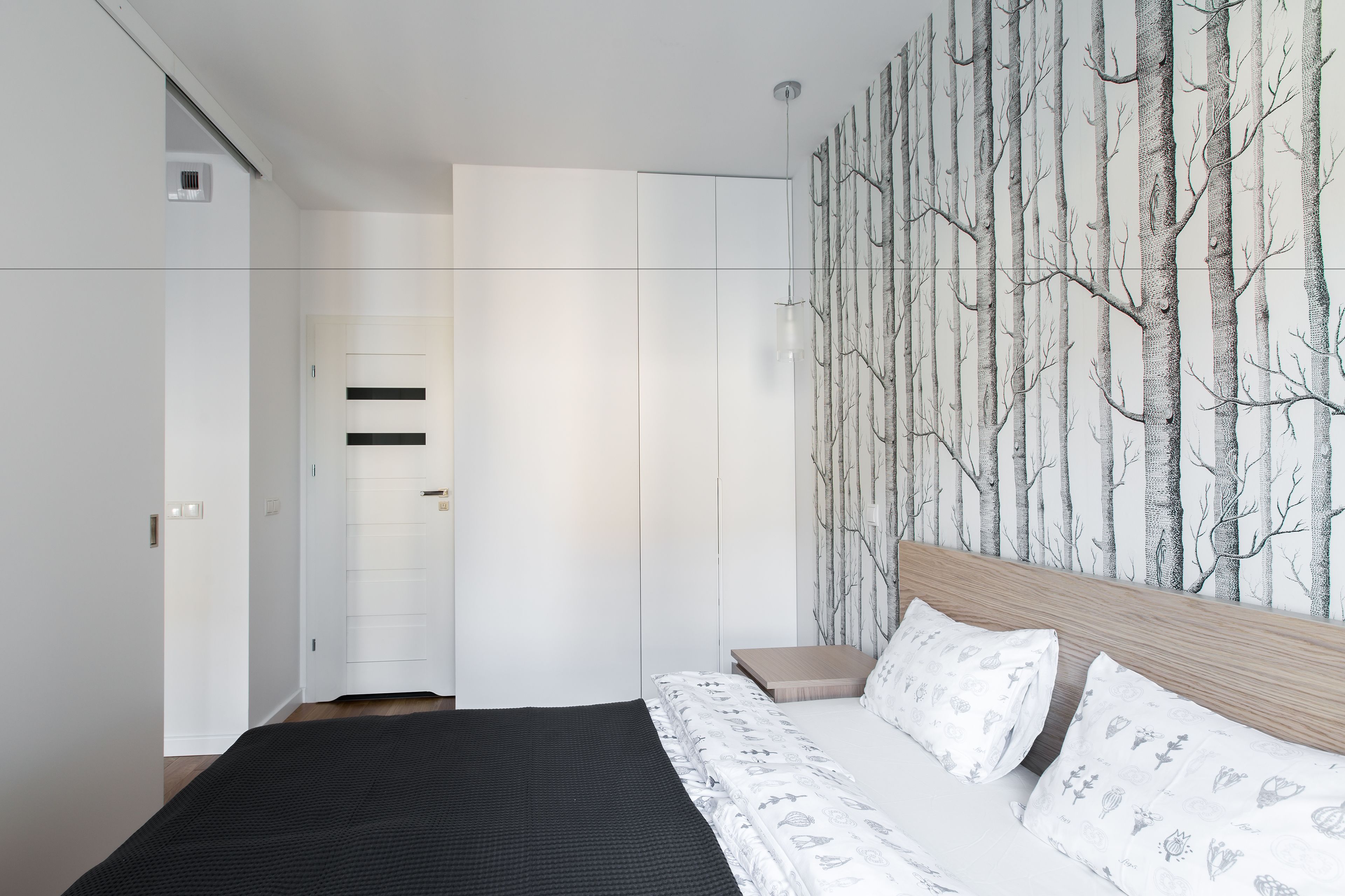 A bedroom with a bed, a wardrobe, and a wall with a tree pattern.
