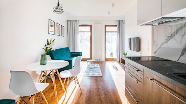 A modern kitchen with wooden cabinets, a black countertop, and a built-in stove. There is a dining area with a white table, two chairs, and a blue sofa. - Homewell Apartments Dominikańska (Poznan)