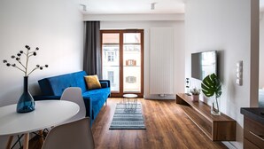 A modern living room with a blue sofa, a white dining table, and a large window with a view of buildings. - Homewell Apartments Dominikańska (Poznan)