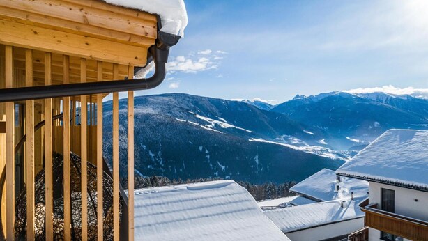 Een houten balkon met een met sneeuw bedekte kap, met uitzicht op een bergachtig landschap.