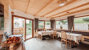 Een eetgedeelte met houten tafels en stoelen, een houten plafond en grote ramen met gordijnen.