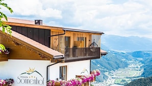 Hotel met uitzicht op bergen, een houten gevel, een balkon met panorama en een bordje dat aangeeft dat het een pension is.